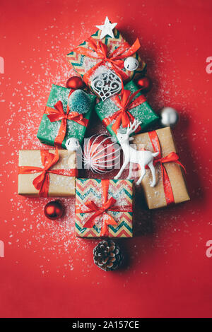 Christmas tree made with gift boxes and Christmas ornaments on a red background with snow. Flat lay Stock Photo