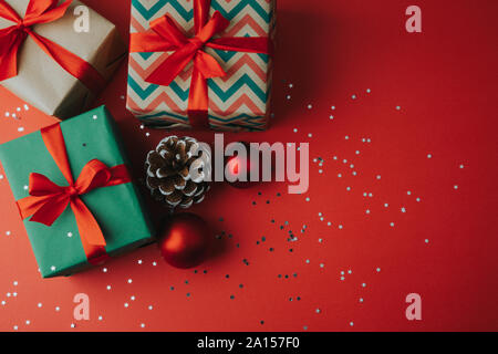 Christmas gift boxes with pine cone, ornaments and star shaped glitter on a red background. Flat lay Stock Photo