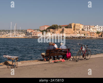 Three people sitting on a bench in the harbour in Chania, Crete Stock Photo