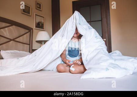 Cute little girl hiding under her blanket on a big bed at home. Home games. Happy childhood. Good morning concept. Stock Photo