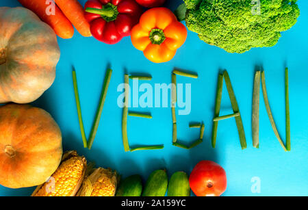 Frame of fresh vegetables with vegan word on blue background. Vegan word made of green onion. Stock Photo