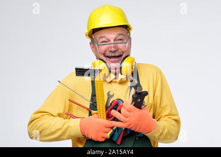 Laughing senior hispanic plumber in protective glasses, gloves and helmet holding tools in hands. Studio shot Stock Photo