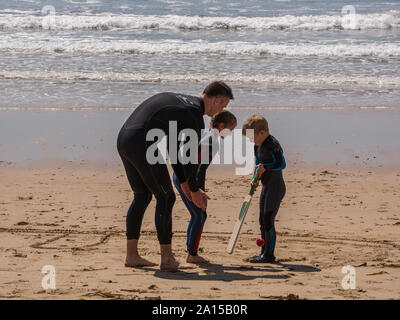 A father and two sons playing cricket on the beach Stock Photo