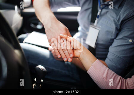 Male auto instructor takes exam in young woman. Shaking hands. Sit together in car. Daylight outside. Agreement. Pass exam Stock Photo