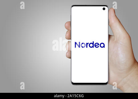 A man holds a smartphone displaying the logo of company Nordea listed on OMX Stockholm. Grey gradient in the background. Credit: PIXDUCE Stock Photo