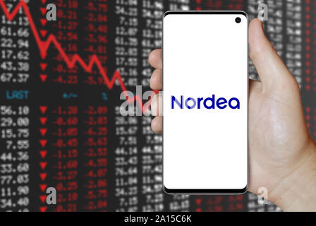 A man holds a smartphone displaying the logo of company Nordea listed on OMX Stockholm. Negative stock market background. Credit: PIXDUCE Stock Photo