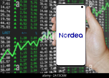 A man holds a smartphone displaying the logo of company Nordea listed on OMX Stockholm. Positive stock market background. Credit: PIXDUCE Stock Photo