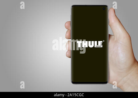 A man holds a smartphone displaying the logo of company Thule