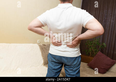 Lower back pain. Man in white shirt holding his back in pain Stock Photo