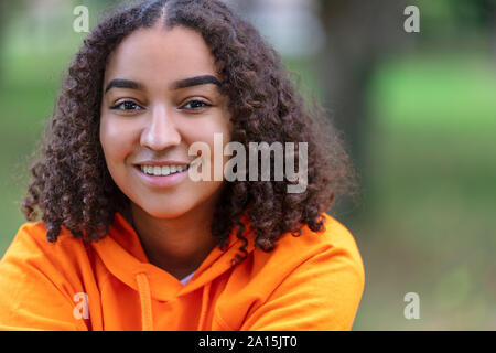 Outdoor portrait of beautiful happy mixed race biracial African American girl teenager female young woman smiling with perfect teeth and wearing an or Stock Photo