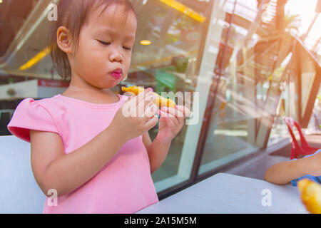 Adorable asian child smiling and enjoy eating breaded sticks at restaurant in her lunch.  High resolution image gallery. Stock Photo