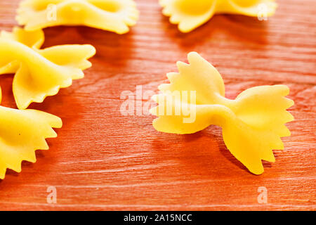 Dry italian pasta called farfalle on wooden red table , beautiful bow tie  -shape pasta Stock Photo