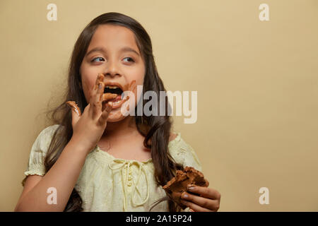 Girl licking chocolate from fingers holding a chocolate bar in the other hand looking away Stock Photo