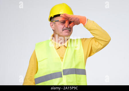 Displeased mature road worker in helmet and protective gloves closes nose because of unpleasant smell. Sewage problem. Stock Photo