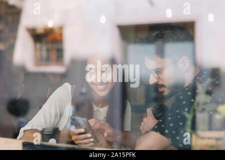 Young couple with smartphone behind windowpane in a cafe Stock Photo