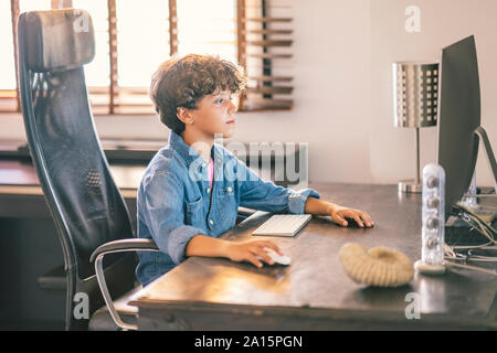 Boy sitting at desk at home using personal computer Stock Photo