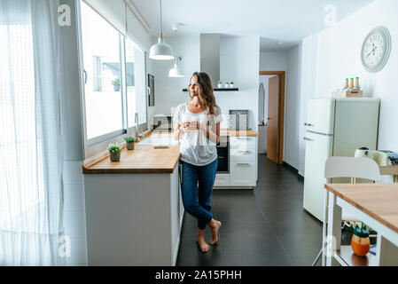Young woman standing in the kitchen with glass of orange juice Stock Photo