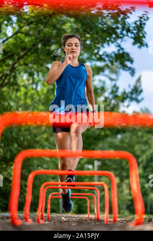 Young woman jumping over hurdles on a woodchip trail Stock Photo