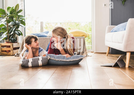 Mother and daughter lying on the floor at home looking at each other Stock Photo