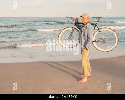 Barefoot man standing with Fixie bike on his shoulder on the beach Stock Photo