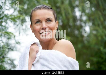 Portrait of smiling woman with wet hair wrapped in a towel in nature Stock Photo