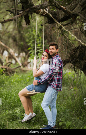 Young woman with boyfriend on a swing in nature Stock Photo