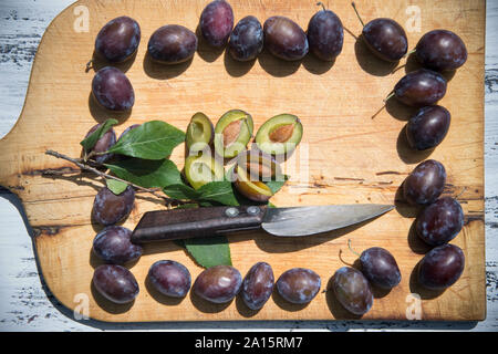Purple plums on wooden cutting board seen from above Stock Photo