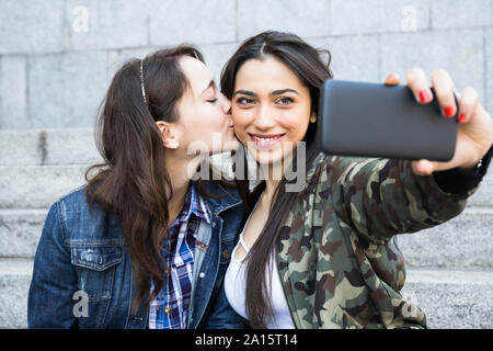 Woman kissing cheek of her friend while she taking selfie Stock Photo