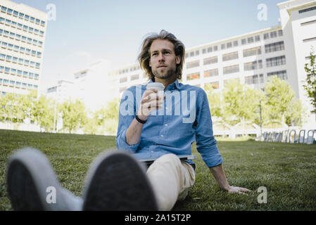 Young man sitting on a meadow with takeaway coffee Stock Photo
