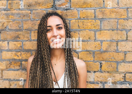 Portrait of happy young woman with long braids in front of brick wall