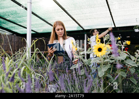 Female worker in a garden center with a tablet caring for flowers Stock Photo