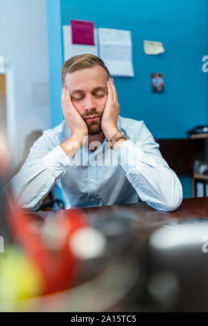 Tired businessman with closed eyes leaning on desk in office Stock Photo
