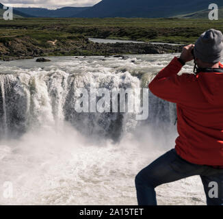 Man looking at Godafoss waterfalls, Iceland, with binoculars Stock Photo