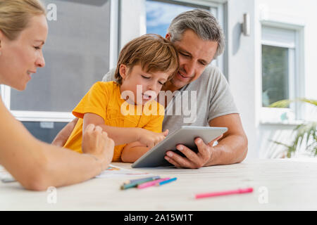 Father, mother and son doing homework and using tablet together on terrace Stock Photo