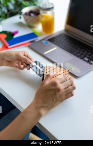 Close-up of woman with laptop taking card out of purse at desk Stock Photo