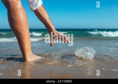 Man standing at seashore picking up empty plastic bottle Stock Photo