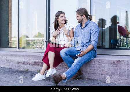 Young couple sitting on windowsill at a building using a tablet Stock Photo