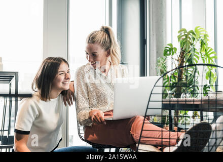 Two happy casual businesswomen with laptop meeting in office Stock Photo