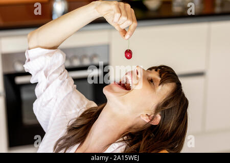 Happy woman eating a cherry in kitchen at home Stock Photo