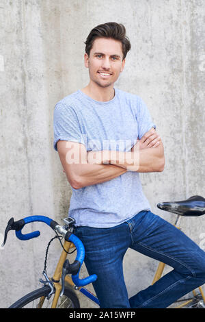 Portrait of smiling man with racing cycle standing in front of concrete wall Stock Photo