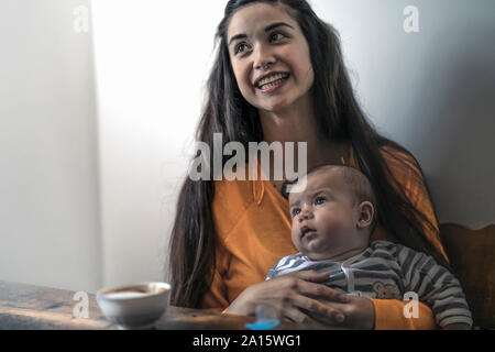 Happy mother with baby sitting at wooden table at home Stock Photo
