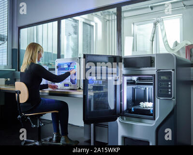 Female technician checking 3D printer with turbine wheel being printed Stock Photo