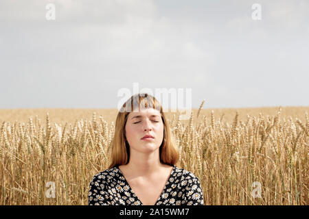 Portrait of young woman with eyes closed relaxing in front of grain field Stock Photo