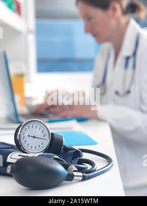 Health check, Doctor examining patients records after a consultation with the focus on a blood pressure gauge Stock Photo