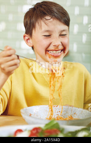 Messy boy eating spaghetti with tomato sauce Stock Photo