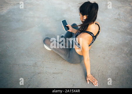 Woman using smartphone and in-ear during workout, sitting on a pier Stock Photo