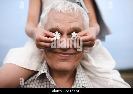 Hands of little girl covering eyes of her grandfather with white blossoms Stock Photo