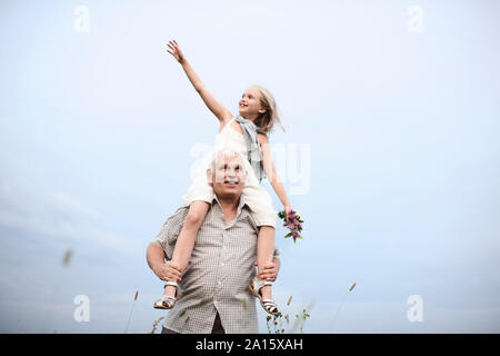 Senior man carrying happy granddaughter on his shoulders in nature