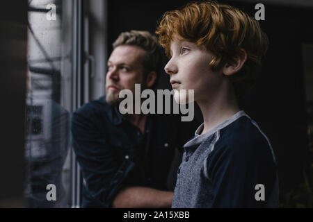 Boy and his father looking out of window on rainy day Stock Photo