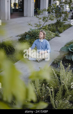 Young man meditating outside office building Stock Photo